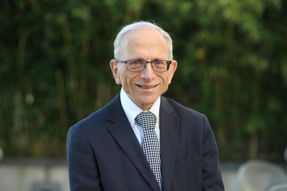 Picture of a man with white hair and glasses wearing a suit smiling at the camera.