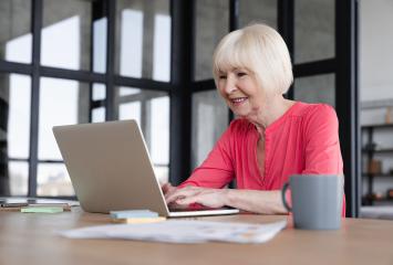 Smiling researcher uses laptop on table with papers and mug nearby