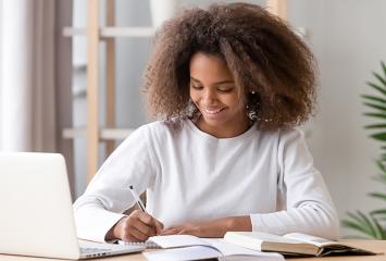 Teenager writing in a notebook next to a laptop