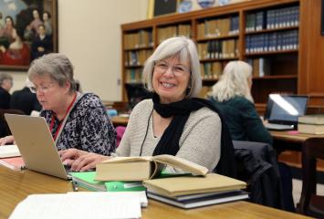 Smiling woman sits with laptop at table in library