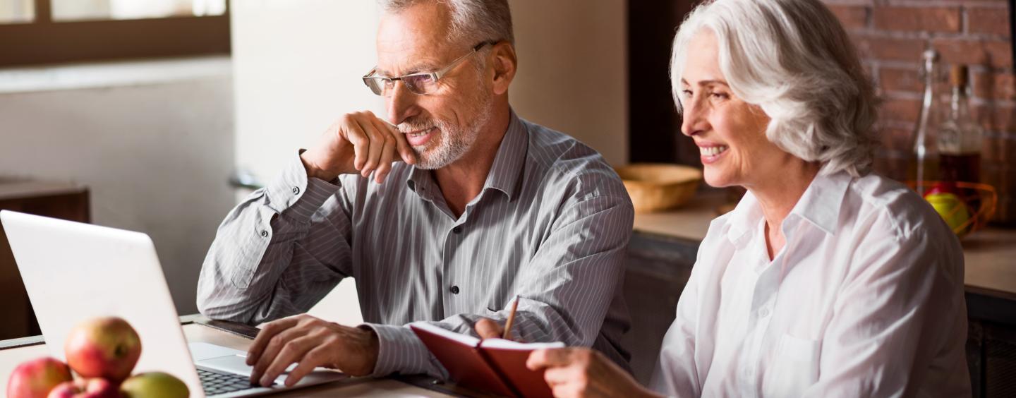 Man and woman use laptop at kitchen table
