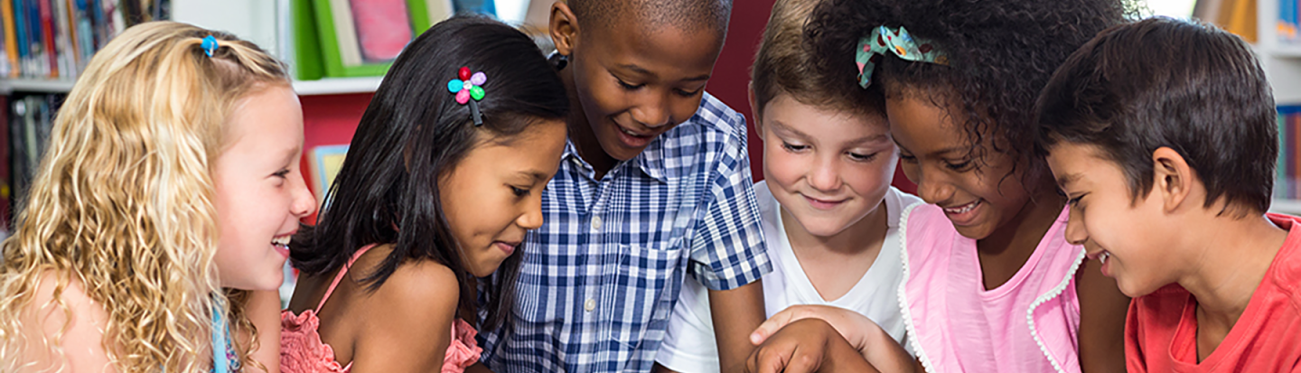 A group of children in a library gather around a tablet computer