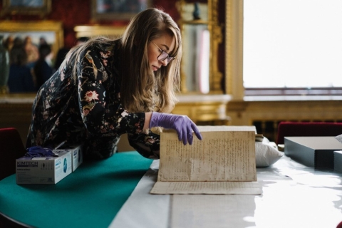 Beckie Burton with blue-ish gloves on turning the page of a historic document