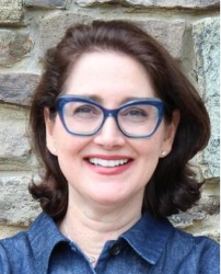 Lisa Krassner, President of the Massachusetts Historical Society, in a blue shirt and glasses photographed before a stone wall