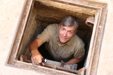 Andrew Lawler climbing up a ladder from a hole, flashlight in hand