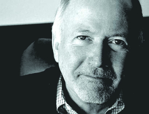 Black and white photo of Bill Griffeth, a man with white hair, a goatee, wearing a sweater and button down. 