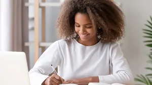 Teenager writing in a notebook next to a laptop