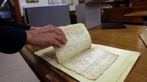 A researcher's hand flips the page of a frayed and fragile, historic document.
