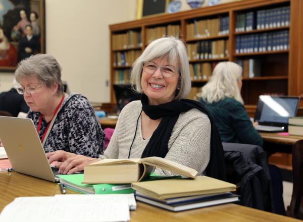 Smiling woman sits with laptop at table in library