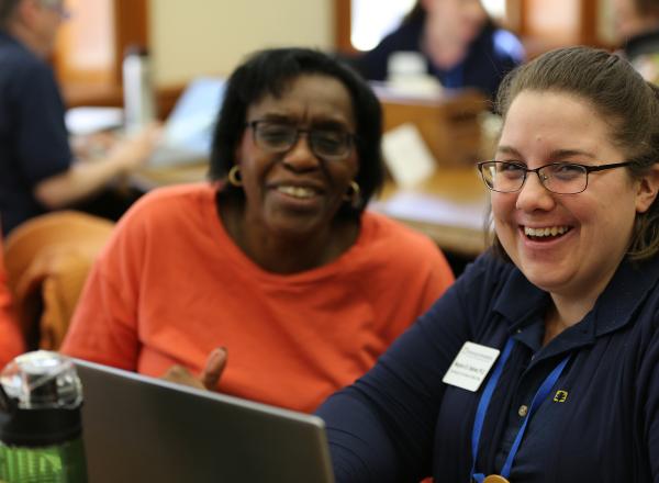 Two women smile while sitting in front of a computer