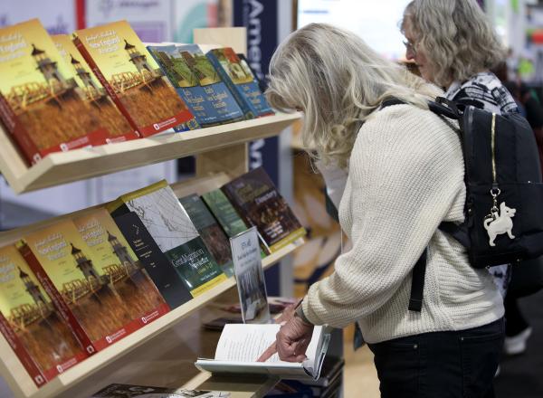 Two women stand in front of a bookshelf. One pages through a book.